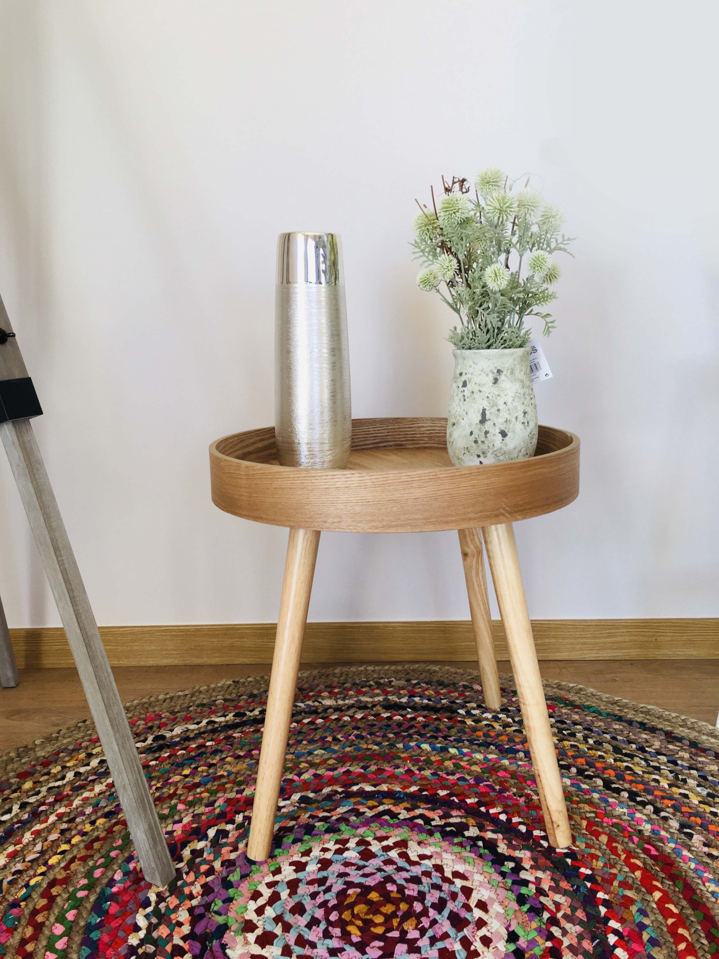 Mesa lateral de madeira com vaso de flores e jarro prateado sobre tapete colorido