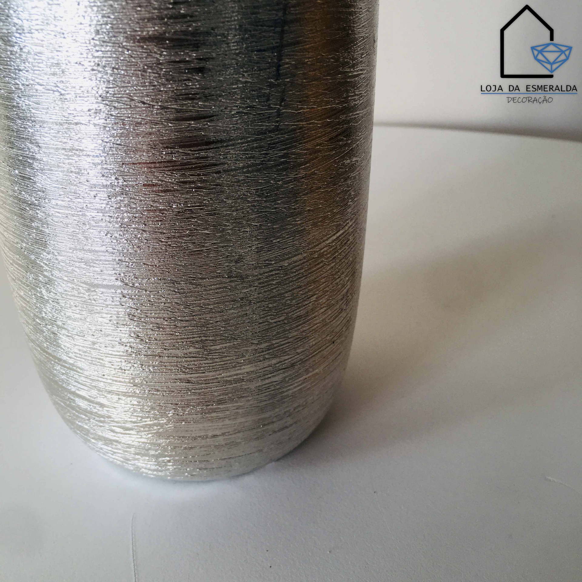 Vaso cilíndrico prateado com textura metálica em fundo branco com logótipo
