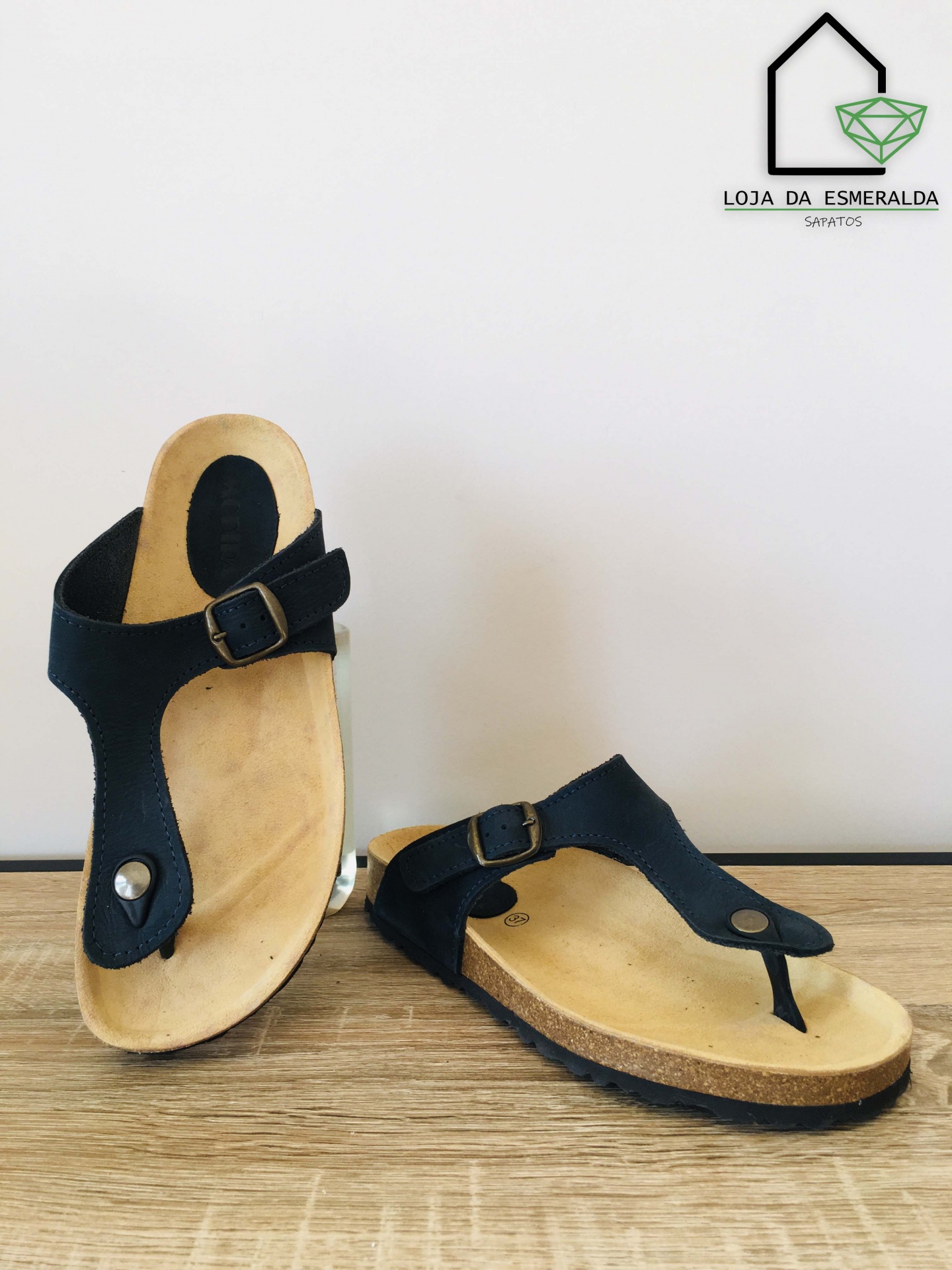 Sandálias femininas pretas com palmilha bege e sola preta em fundo branco e madeira