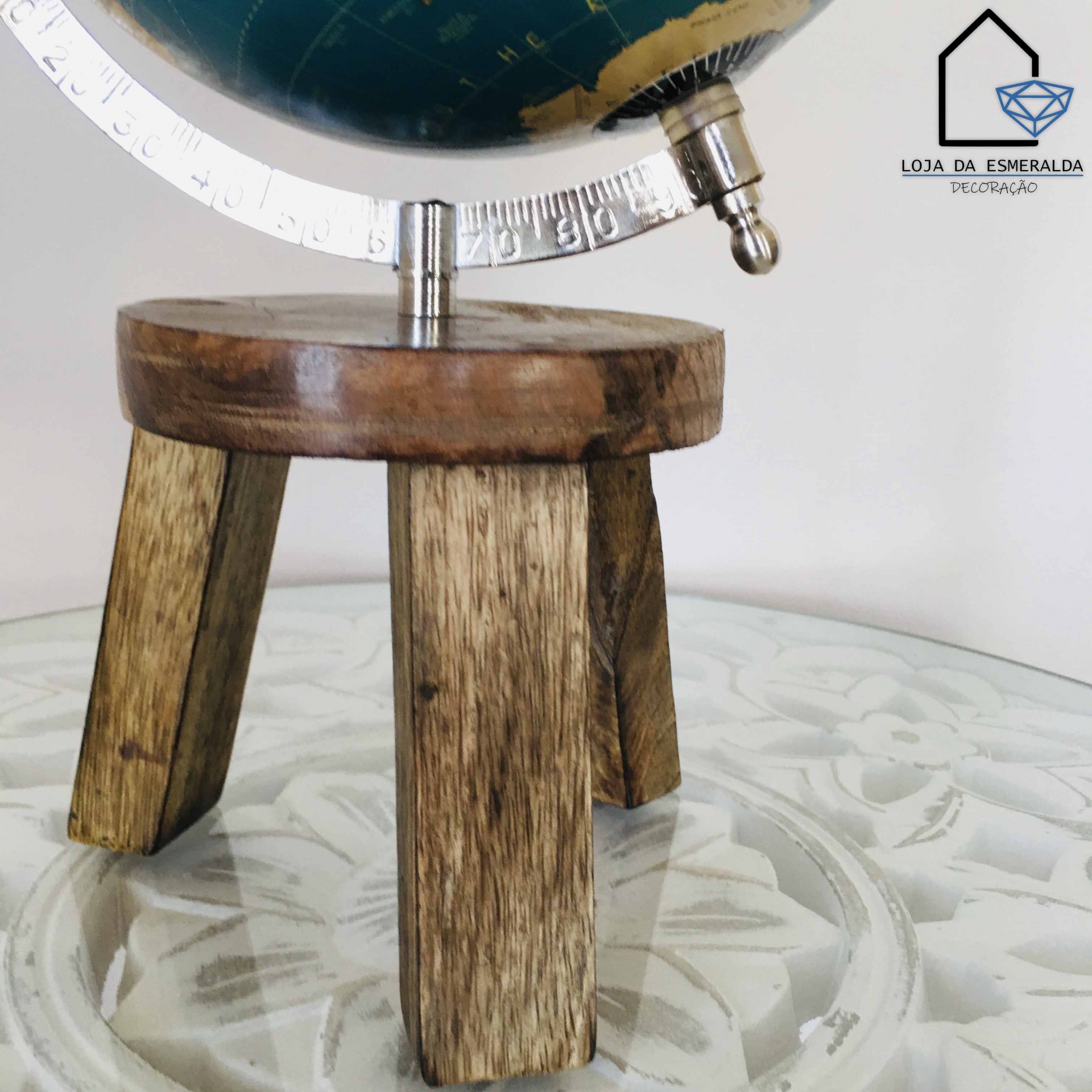 Globo terrestre azul com base de madeira rústica em mesa de vidro com padrão floral.