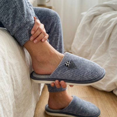 Chinelos cinzentos canelados com detalhes em tecido e piso branco escuro em ambiente doméstico