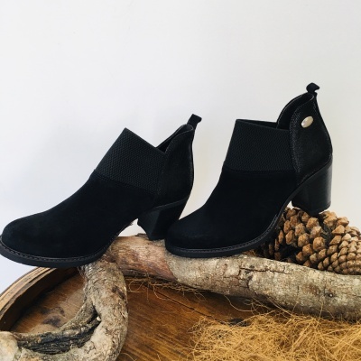 Botins pretos de camurça com elástico e tacão grosso sobre troncos de madeira.