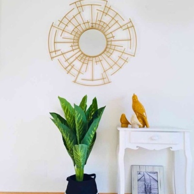 Espelho decorativo dourado, planta em vaso, mesa branca com esculturas e elementos decorativos em ambiente interior.