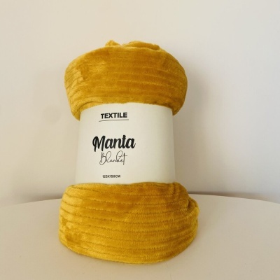 Manta amarela mostarda com etiqueta branca e texto, sobre superfície branca.