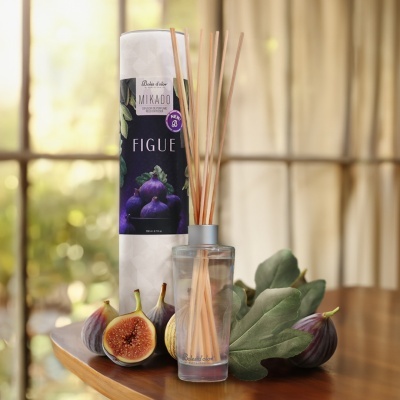 Difusor Mikado com pauzinhos, embalagem decorativa, figos frescos e folhas verdes sobre mesa com luz natural.