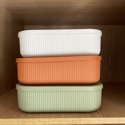 Três caixas retangulares plástico branco, laranja e verde empilhadas em prateleira de madeira