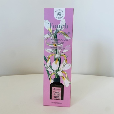 Frasco de difusor de ambiente Touch of Love da La Casa Aromas em embalagem rosa com flores brancas