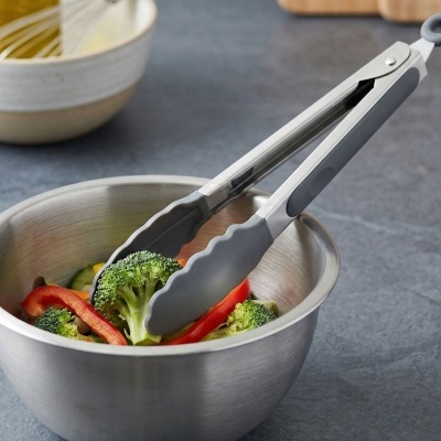 Pegador metálico e silicone cinzento numa tigela de inox com vegetais frescos em bancada cinzenta