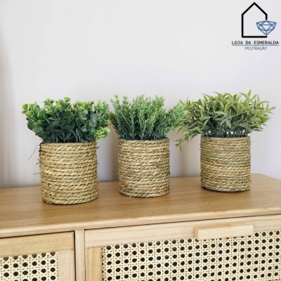 Três vasos de fibras naturais com plantas verdes em cima de móvel de madeira clara com portas de rattan.