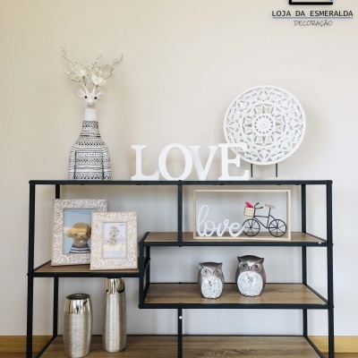 Aparador decorado com objetos em madeira, metal e cerâmica, com logo Loja da Esmeralda Decoração ao fundo