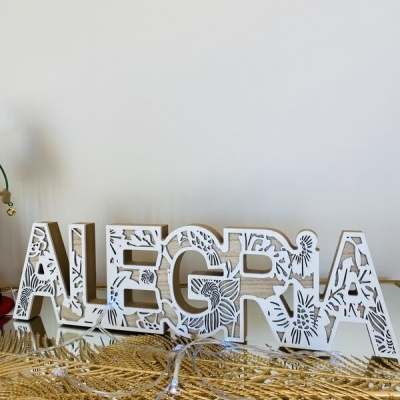 Decoração de mesa em letras de madeira recortadas com padrão floral branco e bege formando a palavra ALEGRIA