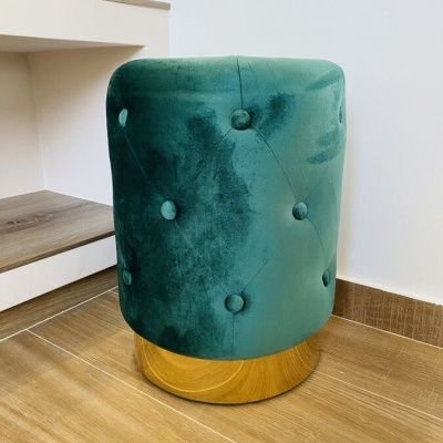 pufe verde aveludado redondo com base em madeira clara em chão de madeira ao lado de secretária branca