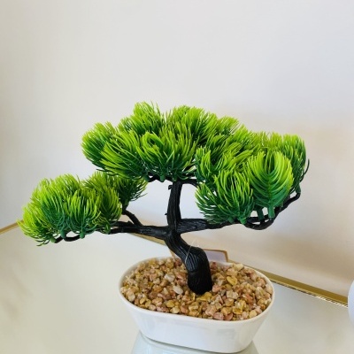 Bonsai artificial com folhas verdes num vaso branco com pedras