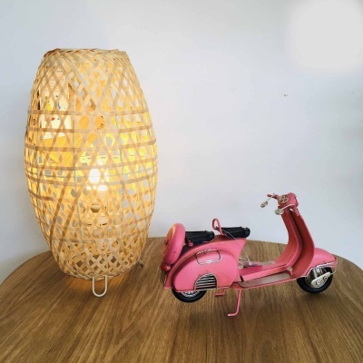 Candeeiro de mesa em vime natural e miniatura de mota rosa numa mesa de madeira