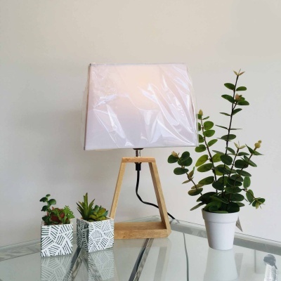 Abajur com base de madeira e cúpula branca, junto a três plantas em vasos em mesa de vidro