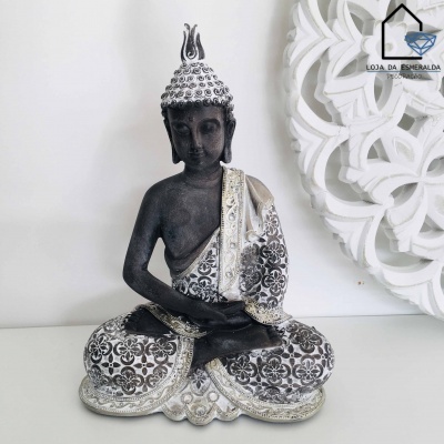 Estátua de Buda decorativa com manto branco e prateado em padrão floral, sobre base branca com fundo claro e decoração branca em relevo.
