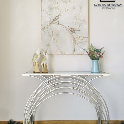 Mesa decorativa branca com pássaros dourados, vaso azul com flores e quadro com pintura de pássaros