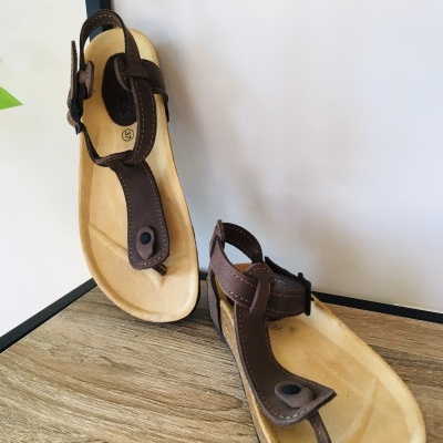 Sandálias castanhas com tiras em couro e sola clara sobre superfície de madeira.