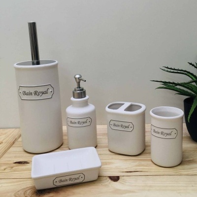 Conjunto de acessórios de casa de banho em cerâmica branca com etiqueta 'Bain Royal' sobre mesa de madeira clara