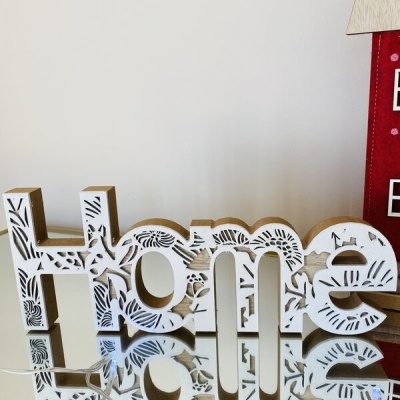 Letreiro decorativo branco em madeira com padrão floral na palavra 'Home' sobre superfície espelhada