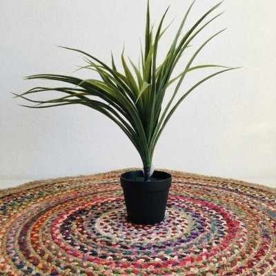Planta artificial em vaso preto sobre tapete redondo colorido
