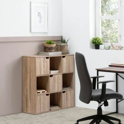 Móvel organizador de madeira clara com compartimentos e plantas num escritório com cadeira e mesa perto de janela