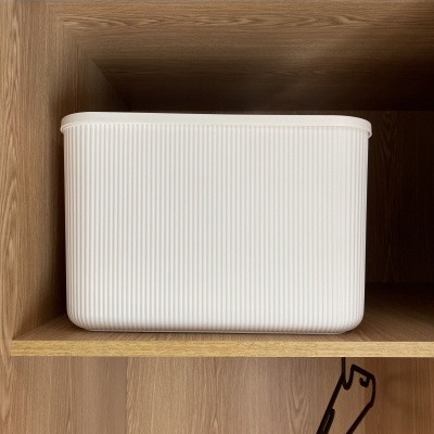 Contentor branco canelado numa prateleira de madeira clara com cabide preto pendurado abaixo.