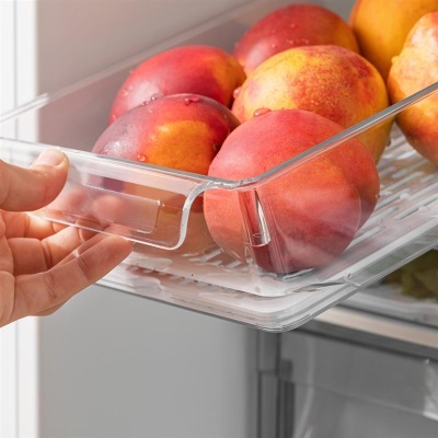 Fruteira transparente com pêssegos dentro de frigorífico e mão a puxar