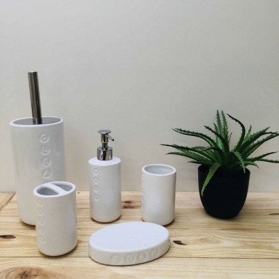 Conjunto de acessórios de casa-de-banho brancos em cerâmica com texto em relevo, sobre tábua de madeira com planta em vaso preto.