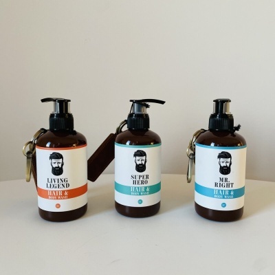 Três frascos de plástico castanhos para cabelo e corpo com tampas de bomba e rótulos coloridos com texto e logotipo de rosto masculino.