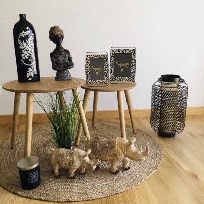 Conjunto decorativo com mesas de madeira, vasos, molduras com escorpião, esculturas de rinocerontes, vela preta e candeeiro metálico num tapete de fibras naturais.