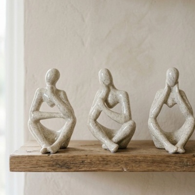 Três estatuetas de figuras humanas abstratas em cerâmica numa prateleira de madeira