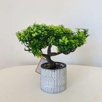 Pequena árvore artificial num vaso decorativo branco com padrão geométrico.