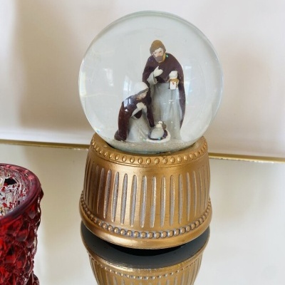 Globo de neve com presépio e base dourada ao lado de objeto vermelho