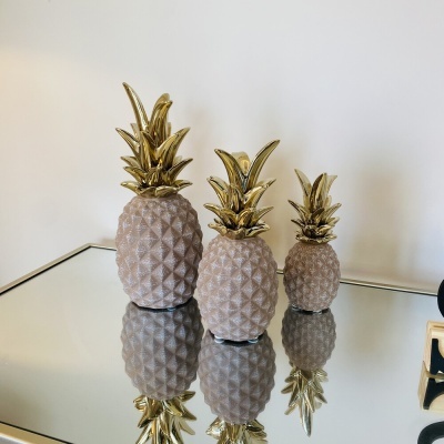 Três esculturas de abacaxi em cerâmica com folhas douradas sobre superfície espelhada