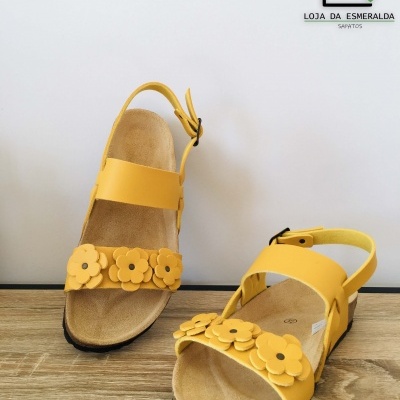 Sandálias amarelas com flores em couro e sola preta sobre madeira