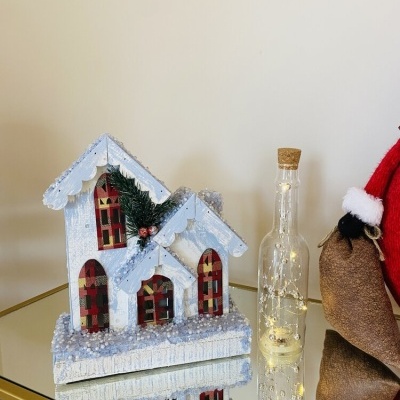 Casinha decorativa de natal com neve artificial e luzes numa garrafa ao lado