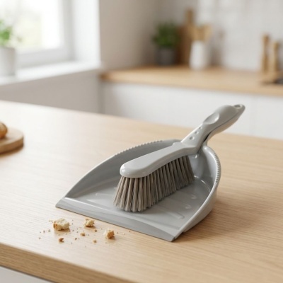 Pá de lixo e escova cinzentas com migalhas sobre bancada de madeira