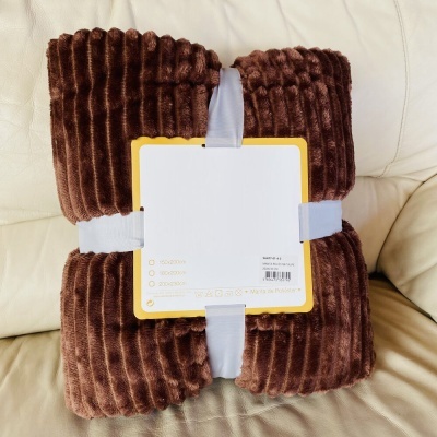 Manta castanha com textura às riscas embalada sobre sofá bege