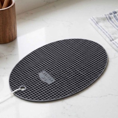 Tapete oval preto texturizado sobre bancada branca com utensílios de cozinha