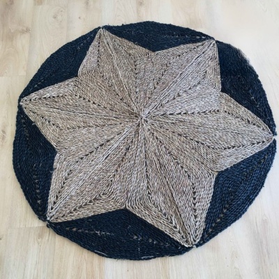 Tapete redondo trançado em padrão de estrela bege e preto sobre chão de madeira clara