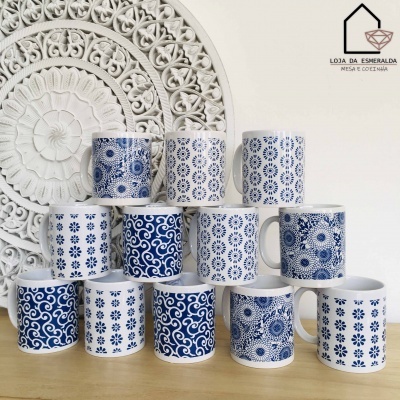 Canecas brancas com padrões azuis em vários designs, dispostas em pirâmide sobre uma mesa de madeira, com decoração branca ao fundo.
