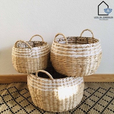 Três cestos trançados naturais com detalhes brancos e alças sobre tapete geométrico