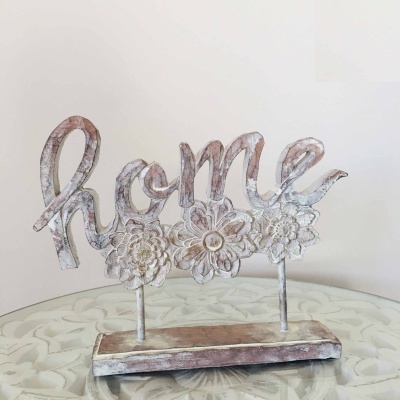 Figura decorativa branca com a palavra home e flores esculpidas sobre mesa de vidro