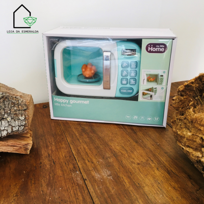 Micro-ondas de brinquedo verde esmeralda e branco em caixa com texto, sobre mesa de madeira