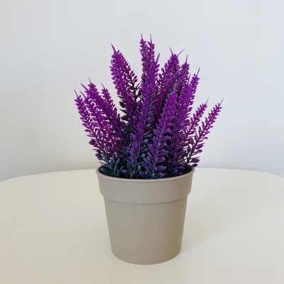 Planta artificial com flores roxas em vaso cinzento claro sobre superfície branca
