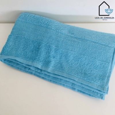 Toalha azul clara dobrada sobre superfície branca com logotipo LOJA DA ESMERALDA