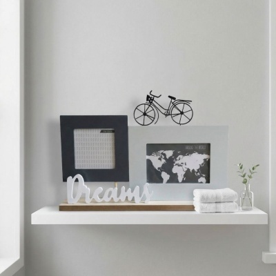Prateleira decorativa com porta-retratos, objeto decorativo com palavra Dreams, mini vaso com planta e toalhas brancas dobradas