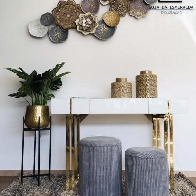 Conjunto de móveis e decoração com aparador branco, dois pufes cinza, vaso dourado com planta e painel floral na parede