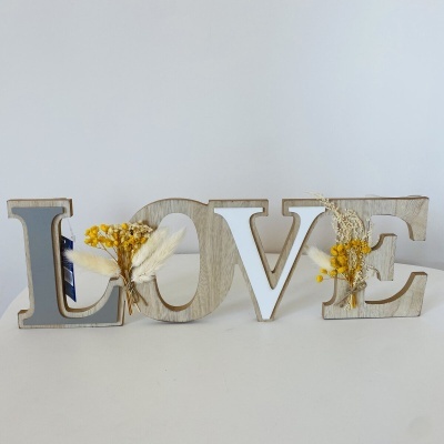 Letras em madeira decorativas formando a palavra LOVE com flores secas amarelas e brancas